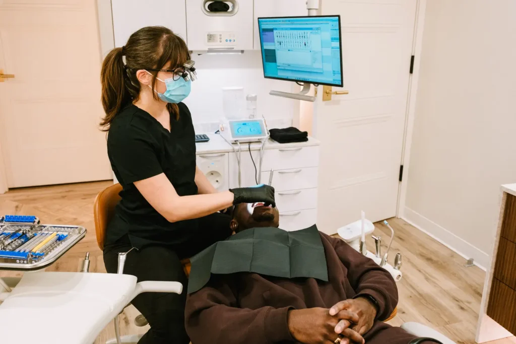 Dental hygienist in scrubs and magnification loupes examining a patient at Vigée Dental