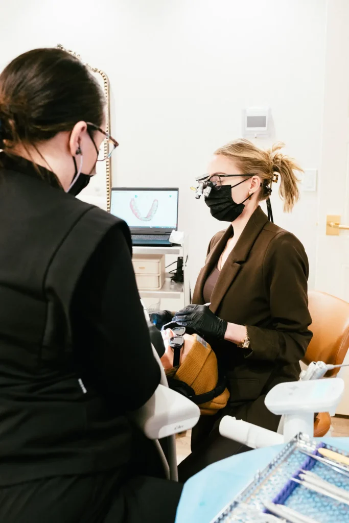 Dentist wearing magnification loupes treating a patient at Vigée Dental, with a digital dental scan on the screen
