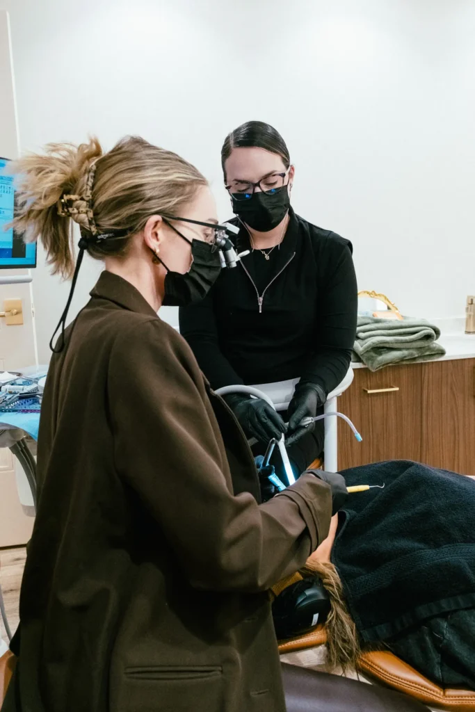 Dentist wearing loupes treating a reclined patient with an assistant beside her